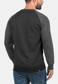 Felpa da uomo in grigio scuro e grigio melange, realizzata in tessuto morbido. Presenta polsini e orlo a coste, maniche raglan e dettaglio del logo.