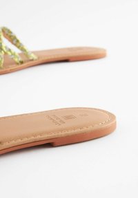 Sandaler i tan färgad läder med dekorativa gröna remmar. Sulan är platt med sömnadsdetaljer och logotypen syns på innersulan.