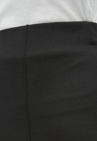 Črna oprijeta krilo iz raztegljive tkanine, z gladko teksturo in vertikalnimi šivi za bolj usklajen videz.