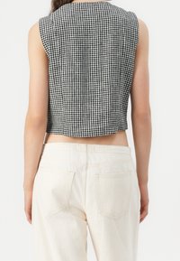 Svart och vit rutigt mönster på en kort topp med rund halsringning och ärmlös design, kombinerad med högmidjade krämfärgade jeans.