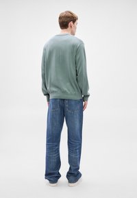 Πράσινο φούτερ με στρογγυλή λαιμόκοψη, συνδυασμένο με άνετα μπλε τζιν. Σημαντικές λεπτομέρειες περιλαμβάνουν ριμπ μανσέτες και τσέπες στα τζιν.