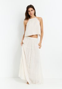 Crop top met halternek in crèmekleurige stof, gecombineerd met een vloeiende rok tot de enkel met verspreide pailletten en een elastische tailleband.