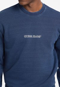 Marineblauwe sweatshirt van gestructureerde stof, met een ronde hals en geborduurd "GUESS JEANS®" logo op de borst.