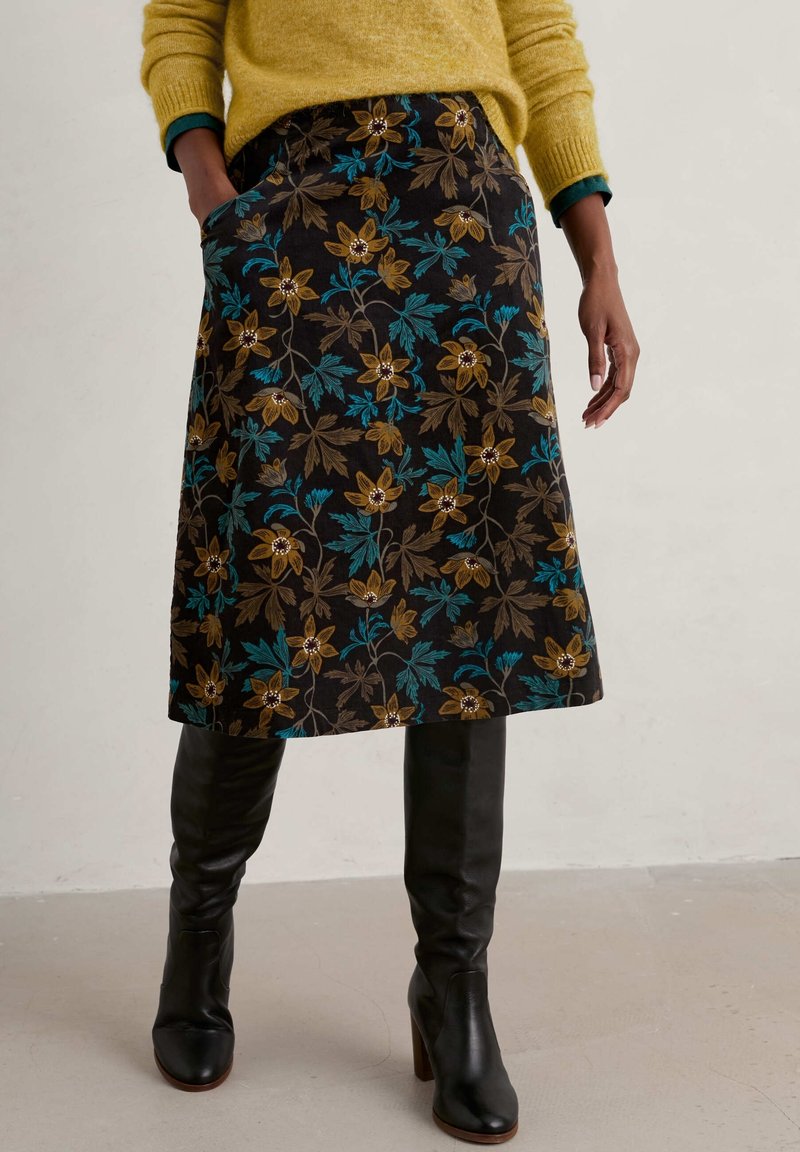 Kwiecista spódnica z ciemnym tłem, ozdobiona wzorami kwiatów w kolorze złotym i turkusowym, uzupełniona czarnymi kozakami za kolano.
