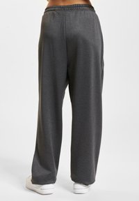 Grå vide joggebukser med elastisk midje, laget av mykt stoff. Kombinert med hvite sneakers, ingen synlige mønstre eller aksenter.