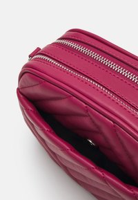 Borsa in pelle fucsia con design trapuntato, dotata di zip argentate e di una tasca interna, che mette in evidenza una consistenza morbida e una forma arrotondata.