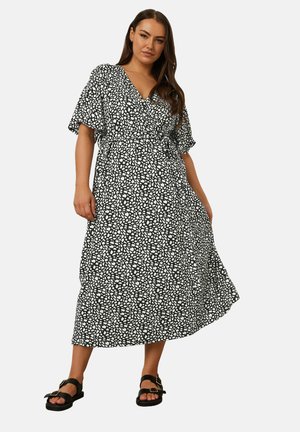 Black and white patterned wrap dress with short, flowy sleeves, a cinched waist, and a mid-calf length, complemented by flat black sandals.