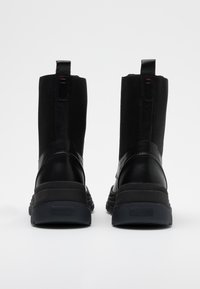Bottes noires à cheville avec tige en cuir lisse et tissu texturé, panneaux latéraux élastiques et semelle en caoutchouc. Design épuré avec des détails minimum.