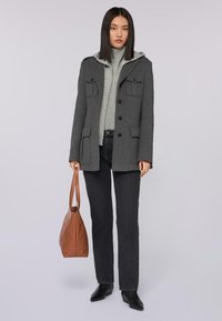 Abrigo de mezcla de lana gris con dos bolsillos frontales, cierre de botones y un suéter con capucha gris claro debajo. Jeans negros y bolso marrón.