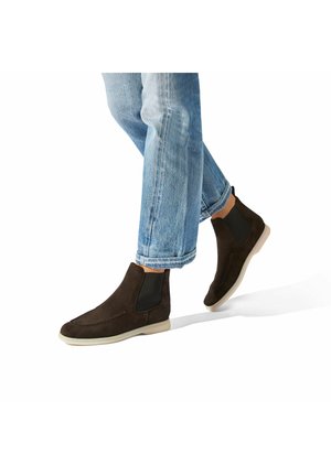 Brune ruskind ankelstøvler med elastiske sidepaneler og hvide gummisåler, parret med rullede blå denimjeans.
