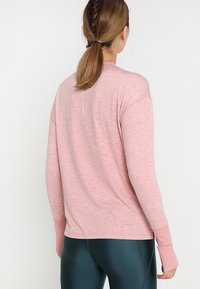 Langarm-Sportshirt in Hellrosa, mit weichem Material, lockerer Passform und dekorativem Nahtdetail auf der Rückseite.