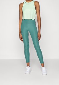 Lichtgroen, cropped sporttopje en teal hoge taille legging, gecombineerd met witte sneakers. Soepele textuur, strakke pasvorm.