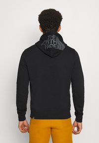 Hoodie noir avec un grand logo ton sur ton sur la capuche. Fabriqué en matériau doux, il présente des manches longues et une coupe décontractée.