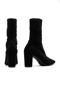 Bottines noires avec une tige en textile ajustée, des talons blocs hauts et une finition lisse, présentant des coutures minimales pour un look épuré.