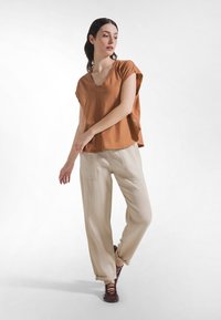 Brun v-hals top med korte ærmer, kombineret med lysebeige, løstsiddende bukser. Mørkebrune snøresko. Blød, afslappet stoftekstur.