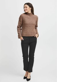 Hnědý žebrovaný rolák vyrobený z texturovaného pleteného materiálu, spárovaný s černými slim-fit kalhotami a černými lodičkami s špičatou špičkou.