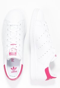 Vita lädersneakers med rosa detaljer på hälen och tungan. Har perforerade sidor och en platt gummisula. Klassisk snördesign.