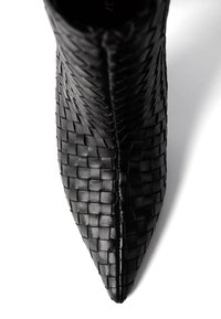 Czarne, plecione skórzane botki za kostkę z wąskim noskiem. Posiadają teksturowane wykończenie oraz gładkie detale po bokach, co tworzy elegancką sylwetkę.
