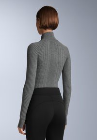 Grå ribbad polotröja med en figurnära design och långa ärmar, kombinerad med svarta höga leggings. Slät, strukturerad yta.