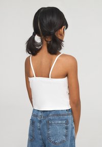Top corto bianco senza maniche con spalline sottili, abbinato a pantaloni shorts in denim blu a vita alta con tasche posteriori e dettagli cuciti.