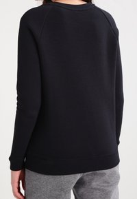 Black sweatshirt with a rounded neckline and raglan sleeves, featuring a smooth texture and elastic hem. Worn with gray sweatpants.