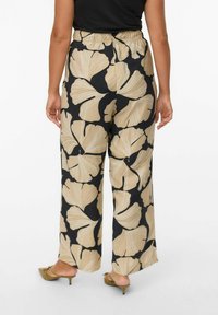 Wide-leg trousers in black with large beige ginkgo leaf pattern. Features an elastic waistband and a smooth texture.