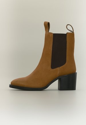Stivaletto in suede marrone con pannello laterale elastico nero e linguette, caratterizzato da un tacco nero spesso di media altezza e punta arrotondata.