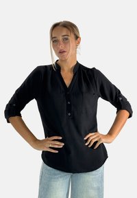 Camicia nera con colletto alla cinese, maniche arrotolate, tasca sul petto e vestibilità comoda. Il tessuto sembra leggero e texturizzato.