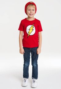 Red short-sleeve T-shirt with a yellow lightning bolt logo on a white circle, paired with blue jeans and white sneakers. Red beanie included.