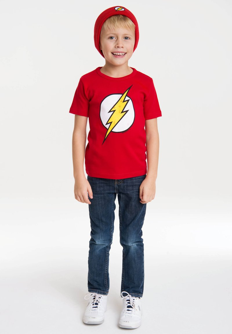 Red short-sleeve T-shirt with a yellow lightning bolt logo on a white circle, paired with blue jeans and white sneakers. Red beanie included.