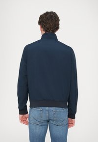 Μπουφάν bomber σε ναυτικό μπλε με όρθιο γιακά, ριμπ μανσέτες και τελείωμα; διαθέτει απαλή υφή και μινιμαλιστικό σχεδιασμό.