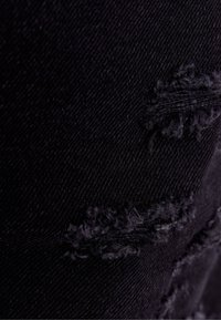 Tissu en denim noir avec des patches usés et des bords effilochés, présentant une texture lisse et un tissage serré.