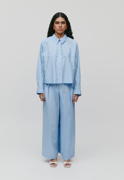 Camicia button-up a righe blu con design cropped, abbinata a pantaloni larghi a righe blu coordinate. Tessuto morbido e polsini larghi.
