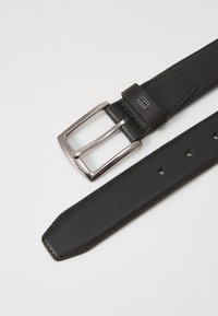 Curea neagră din piele cu o cataramă rectangulară argintie, având o textură netedă, găuri perforate pentru ajustare și un capete îngustat.