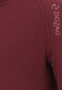 Bordeaux langemouw top gemaakt van een gladde stof, met een getailleerd ontwerp en een klein "ZIGZAG" logo gedrukt op de schoudernaad.