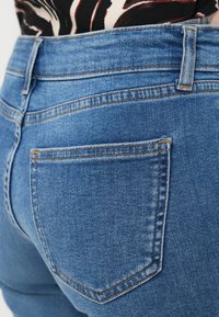 Μπλε τζιν παντελόνι από ντένιμ με κοντινή λήψη της πίσω τσέπης. Διαθέτει κλασικό κόψιμο, εμφανή ραφές και λεία υφή.