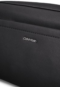 Sort clutch i syntetisk materiale med tekstureret finish. Har et hævet Calvin Klein-logo i sølv. Ren, minimalistisk design uden ekstra metaldele.