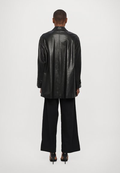 Giubbotto di pelle nera con una vestibilità rilassata, caratterizzato da una cucitura a yoke sul retro, colletto a punta e polsini con bottoni, abbinato a pantaloni neri a gamba larga.
