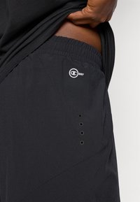 Pantalones cortos atléticos negros con cintura elástica, que presentan un logotipo en el lateral, agujeros de ventilación y una textura de tela suave y ligera.