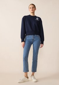 Felpa blu navy con collo rotondo e polsini a costine. Presenta un design con logo sul davanti. Abbinata a un paio di jeans dritti azzurri e sneakers.