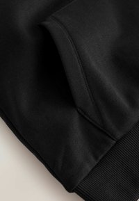 Un hoodie noir à la texture de tissu lisse, avec des poignets côtelés et une poche kangourou avec des coutures renforcées pour plus de durabilité.