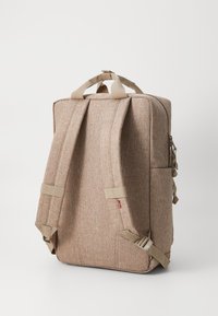 Mochila de tela beige con una apariencia texturizada, que cuenta con correas ajustables, un asa en la parte superior y un bolsillo lateral con detalle de cremallera.