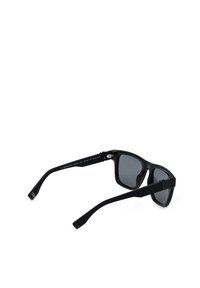 Lunettes de soleil à monture en plastique noir avec des verres teintés foncés, affichées en angle sur fond blanc.