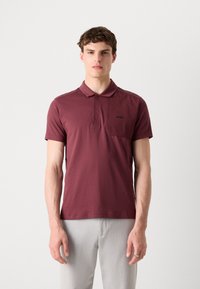 Bordový polo tričko s krátkymi rukávmi, zapínaním na dve gombíky a malou náprsní kapsičkou. Na kapsičke sa nachádza nenápadné logo, vyrobené z bavlneného zmesi.