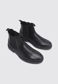 Botas Chelsea de cuero negro con paneles laterales elásticos, lengüetas de tira, punteras redondeadas y suelas de goma texturizadas. Acabado suave con un detalle mínimo.