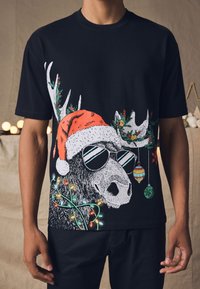 Black t-shirt featuring a graphic of a moose wearing sunglasses and a red Santa hat, adorned with holiday lights and ornaments.