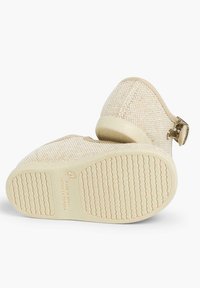 Zapatos de tela beige con un tejido texturizado, punta redondeada y suela de goma con un patrón estriado. Cremallera lateral y detalles en hardware plateado.