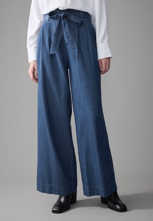 Denim vide bukser i mørkeblå med bælte i taljen, der har en glat tekstur og syet kant, parret med sorte hæleboots.