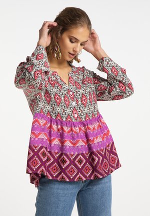 Mnohobarevná blůza s vzorovaným korpusem v růžové a černé barvě, výraznou fialovou vrstvou a dlouhými rukávy s knoflíkovými manžetami.