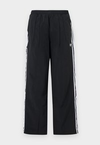 Pantaloni neri a gamba larga con strisce laterali bianche, vita elastica, pieghe frontali e logo Adidas sulla coscia destra.